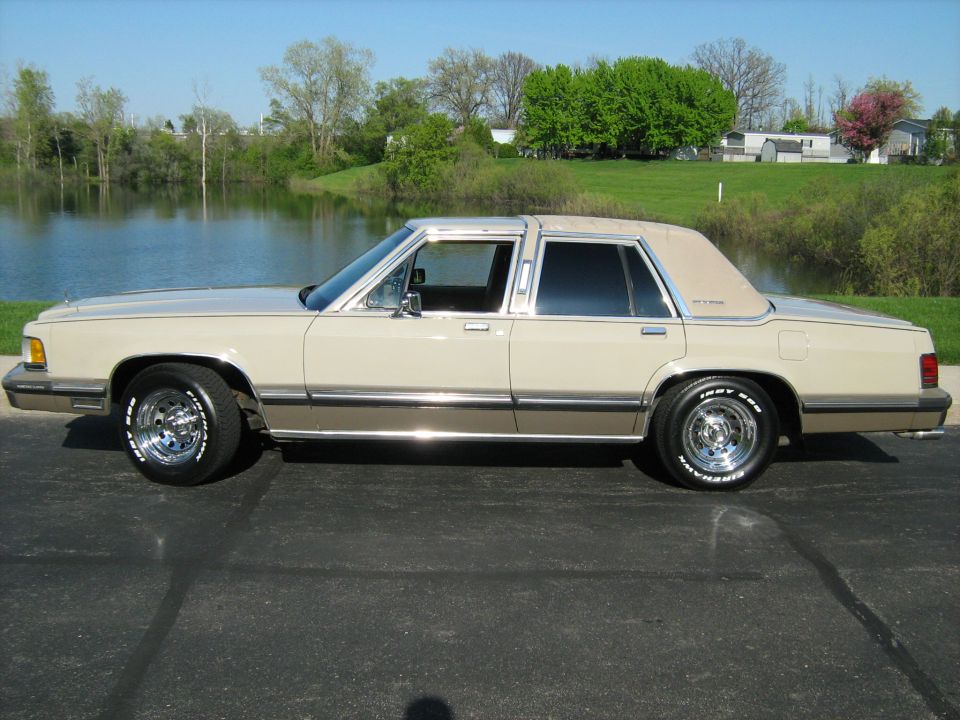 Side view of a tan 1988 Mercury Grand Marquis parked on asphalt near a lake