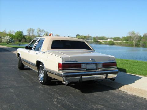 1988 Mercury Grand Marquis - Rear view of a tan 1988 Mercury Grand Marquis sedan parked by a body of water.