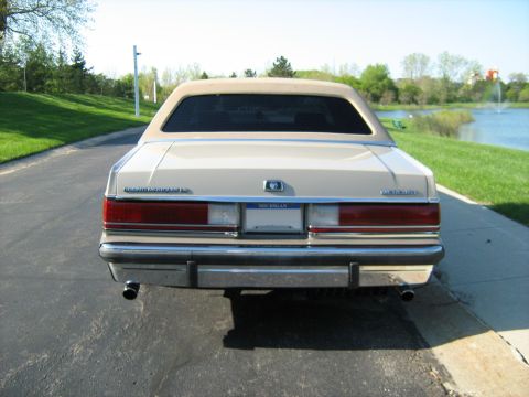 1988 Mercury Grand Marquis - Rear view of a tan 1988 Mercury Grand Marquis with a beige vinyl top, parked outdoors near a body of water.