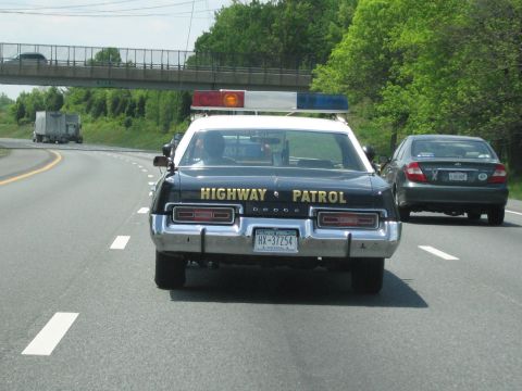 1991 Ford LTD Crown Victoria - rear of a black Dodge Highway Patrol sedan lettered in gold drives beside a gray sedan on a highway under an overpass.