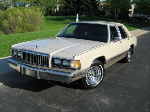 1988 Mercury Grand Marquis - A tan 1988 Mercury Grand Marquis is shown from a three-quarter front view on a sunny day.