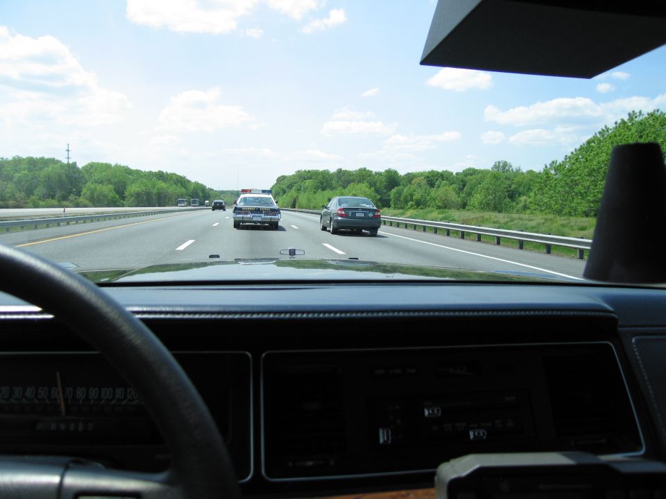 Highway view through a car windshield showing a police car ahead on the road