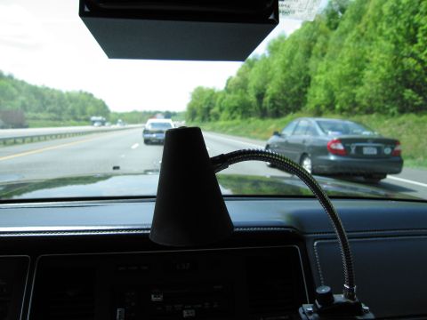 1991 Ford LTD Crown Victoria - black cone-shaped device on a flexible gooseneck mount sits on a dashboard, pointed at highway traffic visible through the windshield.