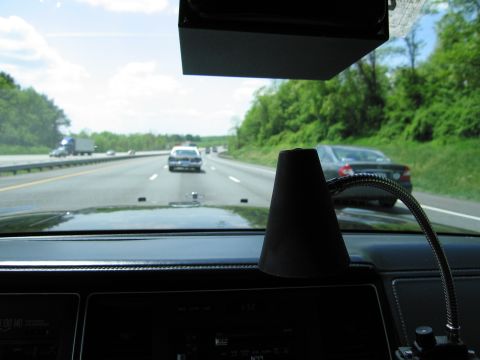 1991 Ford LTD Crown Victoria - black cone-shaped device on a gooseneck arm rests on a car dashboard while traffic and a police car travel the highway ahead.