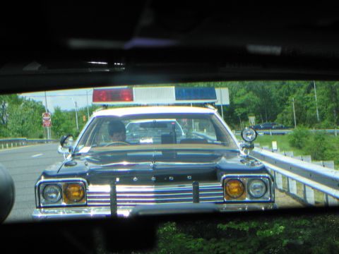 1991 Ford LTD Crown Victoria - black Dodge police cruiser with amber headlight covers and a roof lightbar is viewed through the windshield of a following vehicle.