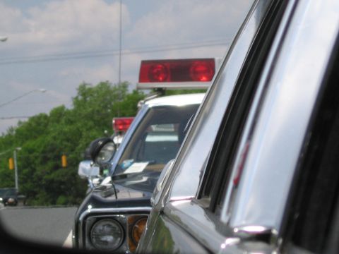 1991 Ford LTD Crown Victoria - Close view of a police cruiser's red roof beacon and front fender, framed by the chrome window frame of an adjacent vehicle.