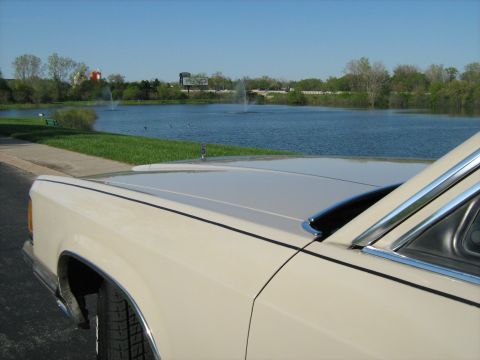 1988 Mercury Grand Marquis - A sedan is parked near a lake with fountains in the background.