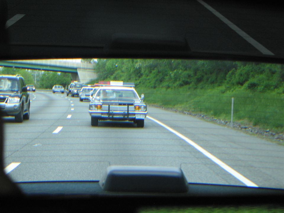Convoy of vintage police cars on a highway seen through a tinted rear window