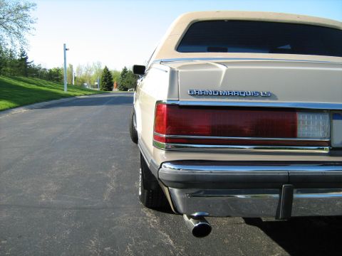1988 Mercury Grand Marquis - Rear view of a cream 1988 Mercury Grand Marquis LS parked on an asphalt road with a grassy embankment.