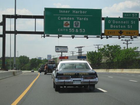 1991 Ford LTD Crown Victoria - black sedan marked HIGHWAY PATROL travels a city highway under green signs for Inner Harbor, Camden Yards and the O'Donnell St/Boston St ex…