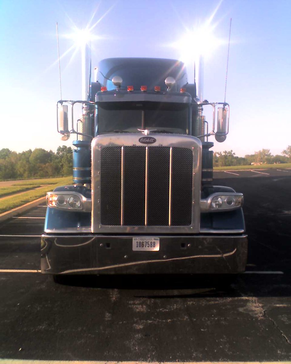 Blue Peterbilt truck front view with chrome grille and headlights. License plate reads 1067588