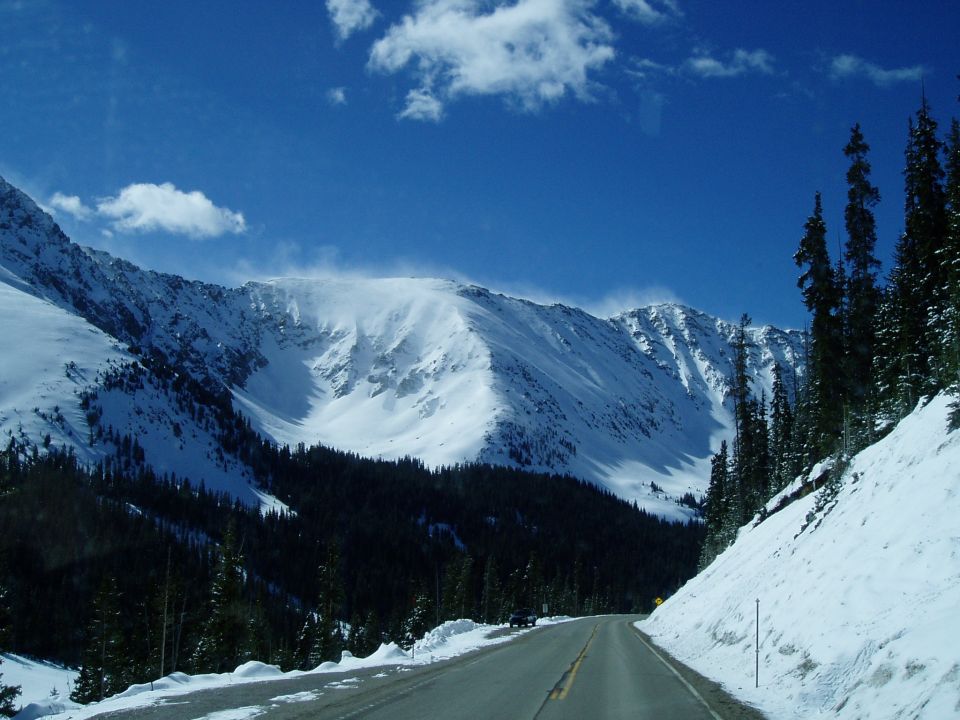 Snowy mountain road with pine trees and blue sky