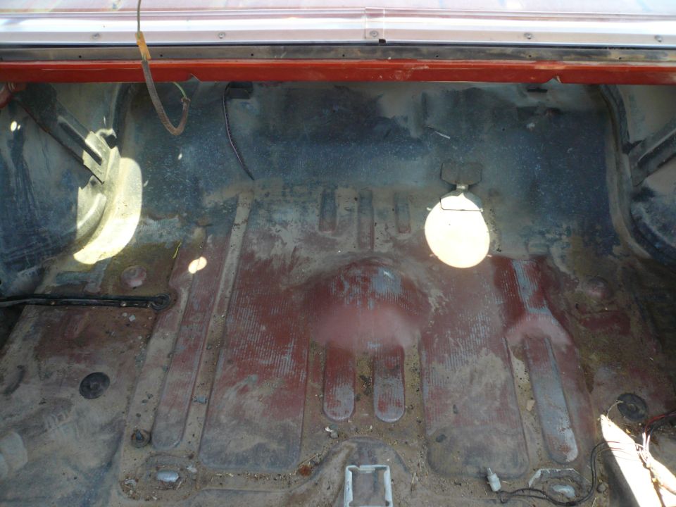 Empty cargo area of a vehicle, showing floor and wheel wells. Some rust and dirt present