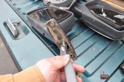 1996 Ford Bronco - A person is working on a vehicle's side mirror assembly, which is disassembled and placed on the truck bed.