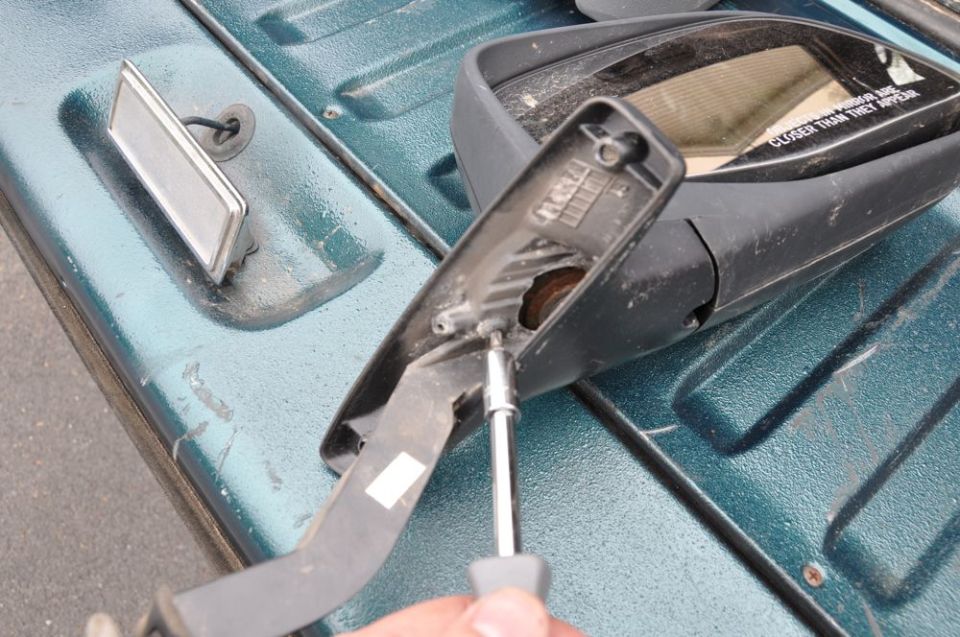 Disassembled side mirror with a screwdriver removing a screw from the housing