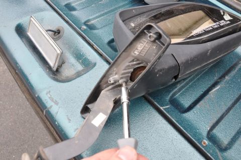 1996 Ford Bronco - A side mirror is being disassembled, resting on the textured surface of a teal vehicle's bed.