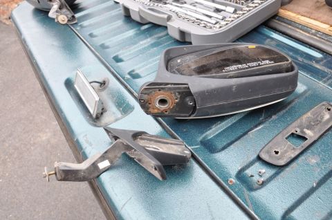 1996 Ford Bronco - A disassembled side mirror assembly, including the mirror housing and mounting bracket, lies on a teal truck bed next to a toolbox.