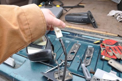 1996 Ford Bronco - A person disconnects the wiring harness from a vehicle's side mirror assembly, with tools and gloves visible in the background.