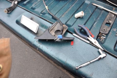 1996 Ford Bronco - A disassembled side mirror, wiring, and various tools are laid out on the bed of a teal truck.