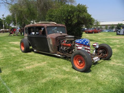 1984 Ford Bronco - A custom-built rat rod with a patriotic theme sits on a grassy field, with other vehicles in the background.