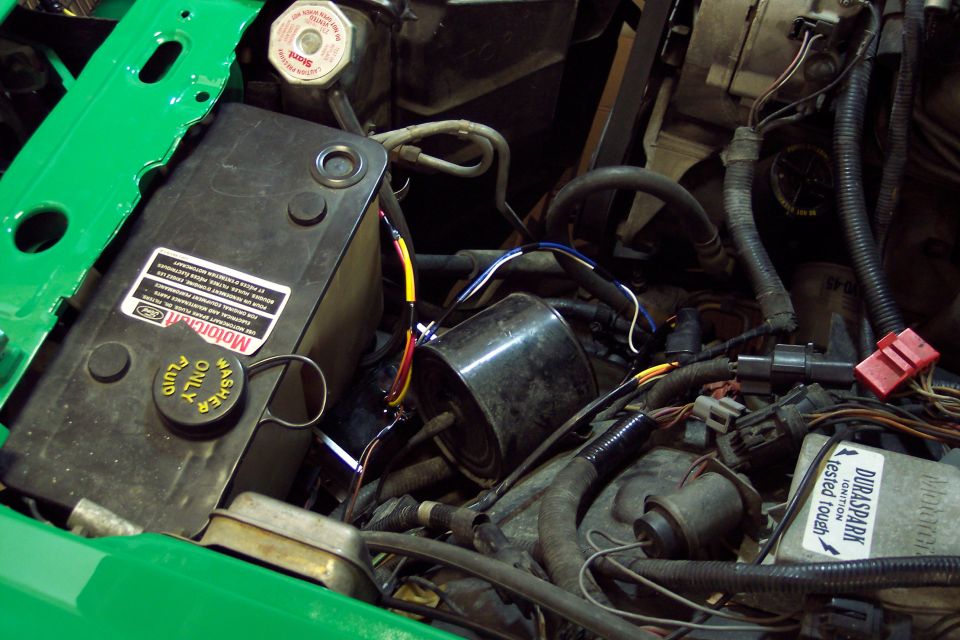 Engine bay with a black fluid reservoir and various wires and hoses. A green painted panel is visible on the left