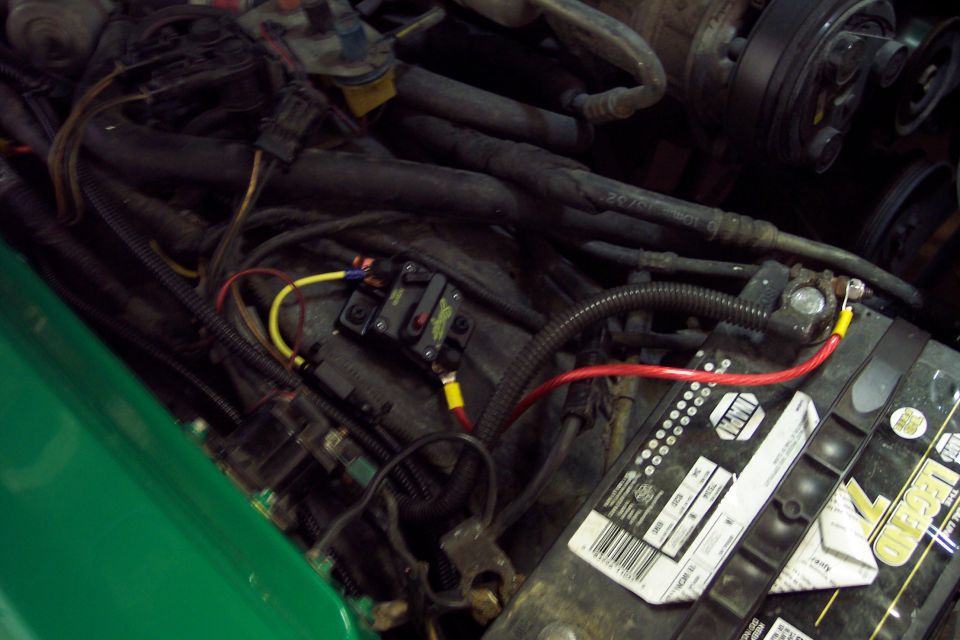 Green fender, car battery, red and yellow wires, and circuit breakers in an engine bay