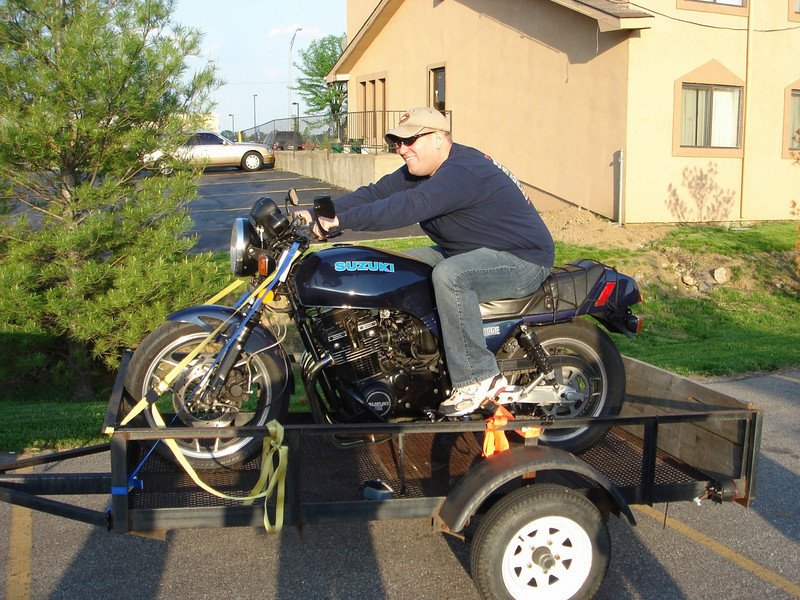 Guy sitting on a dark blue Suzuki motorcycle strapped to a trailer