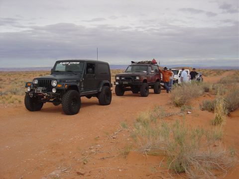 1986 Ford Bronco II - A group of off-road vehicles are stopped on a dusty trail under a cloudy sky.