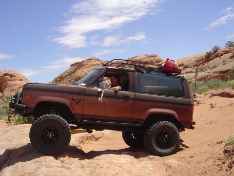 1986 Ford Bronco II - Brown 1986 Ford Bronco II navigating a desert trail with large off-road tires.