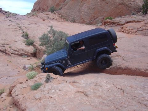 1986 Ford Bronco II - A Jeep Wrangler Rubicon navigates a challenging off-road trail in a desert landscape.