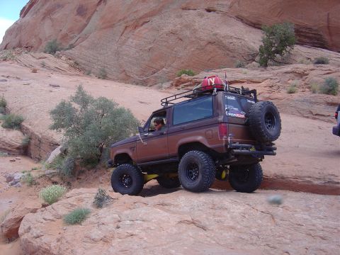 1986 Ford Bronco II - Brown 1986 Ford Bronco II navigates a rocky trail, equipped with a roof rack and spare tire.