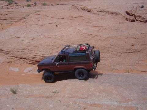 1986 Ford Bronco II - 1986 Ford Bronco II navigates a rocky trail with a roof rack loaded for an off-road adventure.