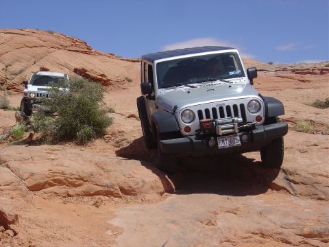 1986 Ford Bronco II - Two off-road vehicles navigate a challenging rocky trail under a clear blue sky.