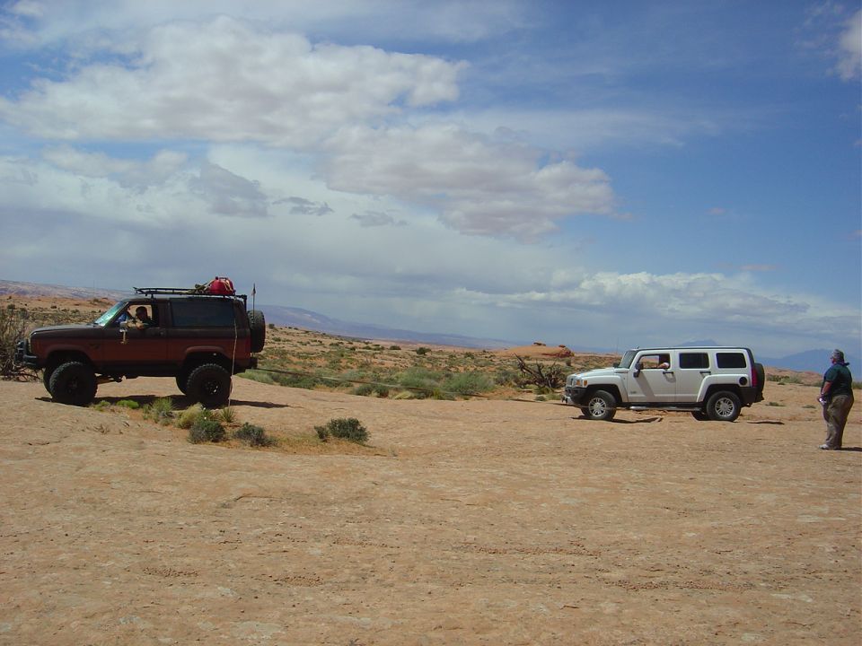 Red Ford Bronco II and white Hummer H3 parked on dirt terrain under a cloudy sky