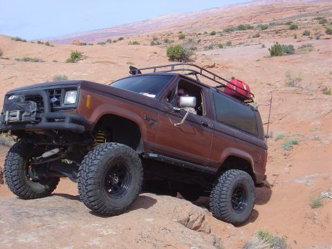 1986 Ford Bronco II - This modified Ford Bronco II navigates a rocky trail in a desert environment, equipped for off-road adventure.