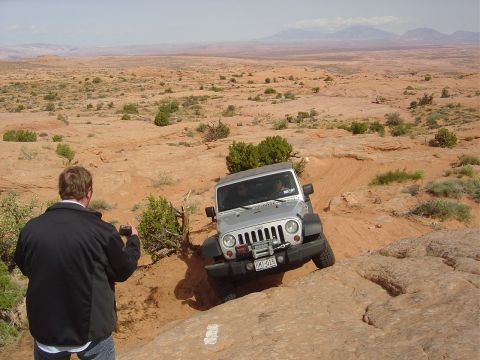 1986 Ford Bronco II - A silver Jeep Wrangler tackles a challenging off-road trail in a desert landscape.