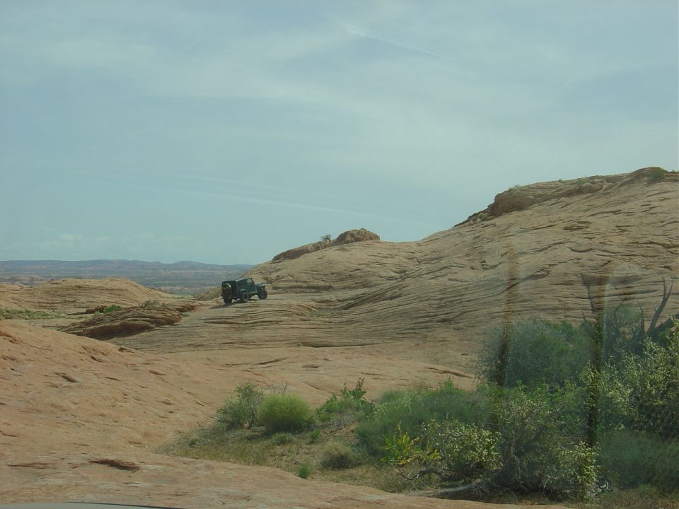 Off-road vehicle driving on a rocky, desert landscape under a cloudy sky