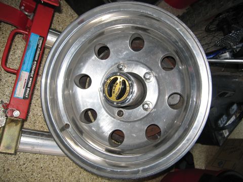 1986 Ford Bronco - Close-up of a Warn locking hub mounted on an aluminum wheel, with a hydraulic wheel dolly visible.