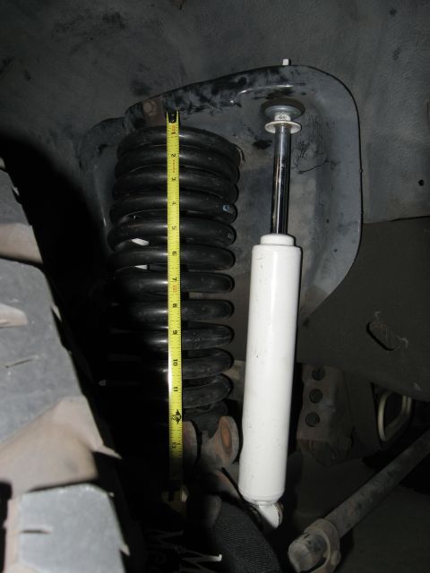 1986 Ford Bronco - Close-up of a vehicle's suspension system, showing a coil spring and shock absorber with a tape measure.