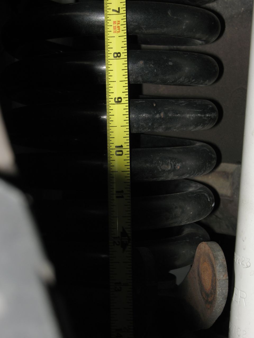 Coil spring measured with a yellow tape measure showing approximately 10 inches