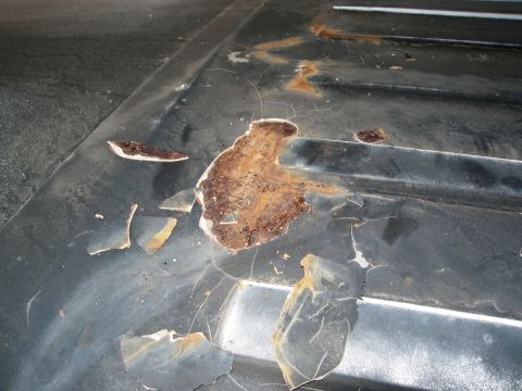 1986 Ford Bronco - Close-up of a damaged vehicle roof panel with significant rust and flaking paint, revealing underlying metal.