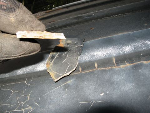 1986 Ford Bronco - A gloved hand peels away a section of paint from a dark vehicle roof, revealing rust and extensive cracking underneath.