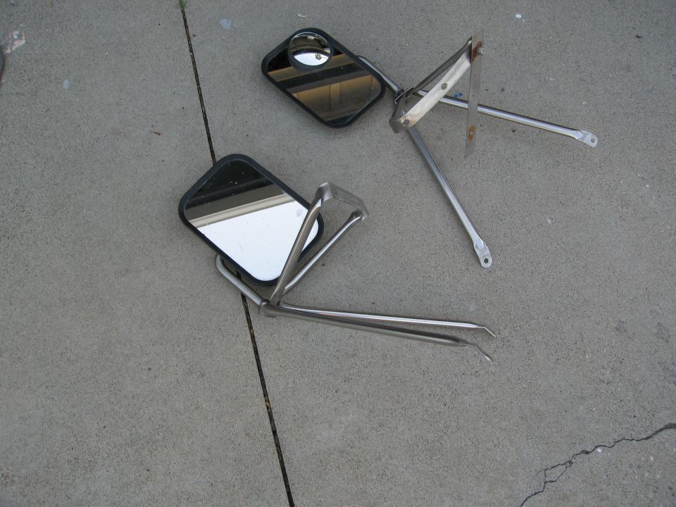 Two side mirrors with chrome mounting arms lying on concrete
