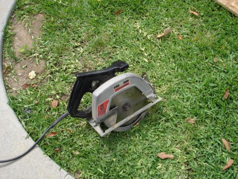 1995 Ford Bronco - A circular saw rests on a grassy area next to a concrete curb. The tool has a silver body and a black handle.