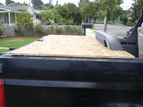 1995 Ford Bronco - Rear of a black full-size Ford with the top removed and gray leather seats visible, hauling a large sheet of OSB particleboard laid flat ac…