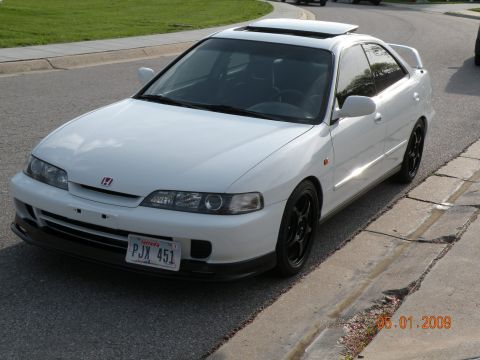 1994 Acura Integra - A white 1994 Acura Integra coupe is parked on the side of the road, a sunroof and black aftermarket wheels.