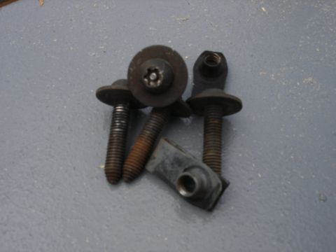 1995 Ford Bronco - Three flanged Torx-head bolts with washer-style heads and two threaded U-nut/weld-nut clips laid out on a gray textured surface. The hardwa…