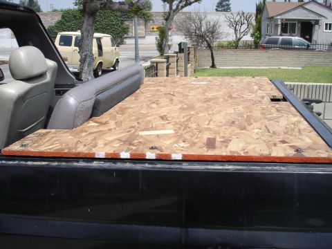 1995 Ford Bronco - View over the rear tub of a black SUV where a cut sheet of OSB particleboard has been fitted as a flat cargo deck over the interior, with t…