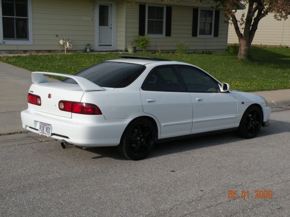 White 1994 Acura Integra sedan with black wheels and a rear spoiler, parked on a street