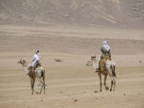 2006 Victory Kingpin - Two people ride camels across a vast desert under a hazy sky.